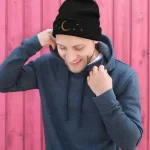 Uomo che indossa una maglietta con stampa astronomica, cappello con luna e stelle, sfondo rosa, stile casual e originale.