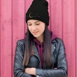 Giovane donna con cappello astronomico nero decorato con luna e stelle, indossa giacca di pelle e sfondo rosa, rappresenta interesse per scienza e astronomia.