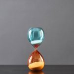 Orologio a clessidra decorativa in vetro blu e arancione, perfetta come oggetto scientifico e decorativo per ambienti moderni e studi di design.