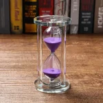Clessidra decorativa in vetro con sabbia viola, perfetta come oggetto scientifico e decorativo, ideale per appassionati di scienza e design.