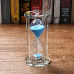 Orologio a sabbia in vetro con sabbia blu, perfetto come decorazione scientifica o oggetto da collezione, simbolo del tempo e della scienza.