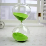Orologio a sabbia con sabbia verde in un ambiente luminoso, ideale come decorazione scientifica o oggetto da collezione, perfetto per appassionati di scienza e design innovativo.