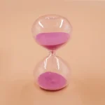 Sabbia rosa che scende lentamente in un orologio di sabbia trasparente, simbolo di tempo e pazienza. Perfetta come decorazione scientifica o oggetto da collezione.