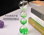 Vaso a clessidra decorativo con sfere di vetro trasparenti e liquido verde, simbolo di tempo e scienza, ideale come oggetto decorativo o da collezione.
