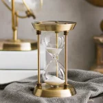 Clessidra decorativa in ottone con sabbia bianca, perfetta come oggetto di design o decorazione scientifica elegante.