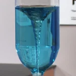 Provetta con liquido blu in movimento, mostra un vortice al suo interno.