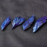 Quattro cristalli di bismuto blu brillante disposti su sfondo nero, evidenziando le loro forme irregolari e la superficie riflettente.