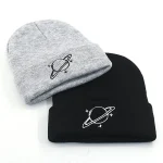 Due cappelli, uno grigio e uno nero, con stampa di un pianeta con anelli, ideali come accessori scientifici e decorativi.