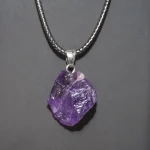 Pendente con cristallo di ametista naturale, gioiello decorativo e simbolico, sospeso su una catena metallica. Perfetto come regalo o accessorio di stile.