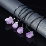Collane con pendenti di cristalli di ametista, perfette come decorazioni scientifiche o accessori eleganti, esposte su un supporto nero lucido.