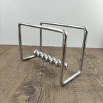Pendolo di Newton in metallo con sfere d'acciaio lucido, oggetto scientifico decorativo per appassionati di fisica e design.