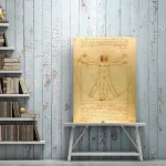 Immagine di un disegno storico di Leonardo da Vinci raffigurante l'Uomo Vitruviano, appeso su una parete in legno bianco con scaffale di libri accanto.