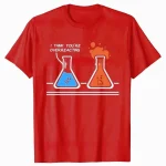 Maglietta rossa con disegno di due beute di laboratorio, una con liquido blu e l'altra con liquido arancione che fuma, con testo "I think you're overreacting".
