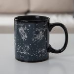 Tazza nera con disegni delle costellazioni zodiacali di Gemelli, Leone, Sagittario e Ariete, con nomi e stelle rappresentate, ideale come decorazione o oggetto da collezione.