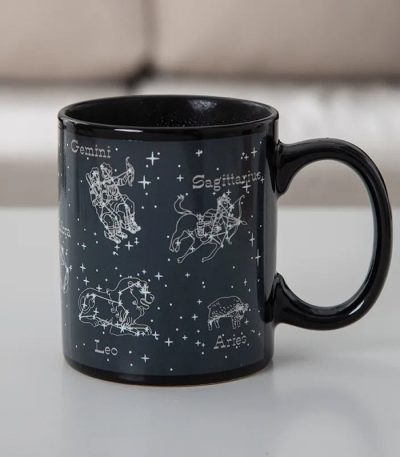 Tazza nera con disegni delle costellazioni zodiacali di Gemelli, Leone, Sagittario e Ariete, con nomi e stelle rappresentate, ideale come decorazione o oggetto da collezione.