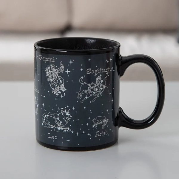 Tazza nera con disegni delle costellazioni zodiacali di Gemelli, Leone, Sagittario e Ariete, con nomi e stelle rappresentate, ideale come decorazione o oggetto da collezione.