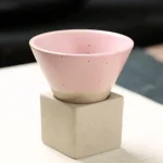 Ciotola decorativa in ceramica rosa su supporto quadrato in cemento, perfetta come oggetto di decorazione scientifica o da collezione.