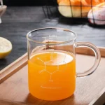 Tazza in vetro con liquido arancione e formula chimica stampata, ideale come decorazione scientifica o oggetto da collezione. Perfetta per appassionati di chimica e decorazioni a tema scientifico.