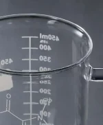 Becher di vetro trasparente con misurazioni in millilitri e linee di livello, ideale per esperimenti scientifici e decorazioni a tema scientifico.