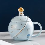 Tazza decorativa a tema spaziale con coperchio a forma di astronauta dorato, perfetta come oggetto da collezione o decorazione per appassionati di astronomia e spazio.