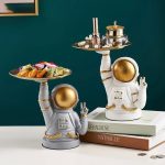 Decorazioni da tavolo a forma di astronauta con vassoi, perfette per ambienti scientifici o tematici, in stile moderno e originale, con dettagli dorati e bianchi.