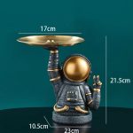 Pupazzo decorativo a forma di astronauta con piatto dorato in equilibrio sulla mano, ideale come oggetto da collezione o decorazione scientifica.