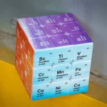 Cubo di metalli e metalloidi della tavola periodica con simboli e numeri atomici, in colori vivaci, su sfondo neutro.