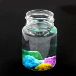 Vaso di vetro con liquido trasparente e pietre colorate, decorazione scientifica per ambienti educativi o decorativi.