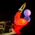 Modello di razzo in volo con scia di fiamme arancioni, accompagnato da una luna luminosa e riflessa in acqua, creando un'ambientazione spaziale e futuristica.