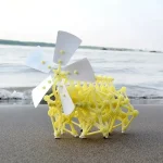 Pale e struttura gialla di un oggetto scientifico decorativo posizionato sulla spiaggia con mare sullo sfondo.