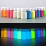 Barattoli di vernice fluorescente in vari colori, visibili sia sotto luce normale che sotto luce UV, ideali per decorazioni scientifiche e artistiche.