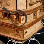 Magnifying glass examining a wooden puzzle box with intricate interlocking pieces.