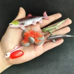 Set di oggetti scientifici in miniatura, tra cui pesci, organismi marini e strumenti di laboratorio, perfetti come decorazioni educative o da collezione.
