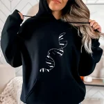 Una donna indossa una felpa con cappuccio nera con un motivo di doppia elica di ADN bianco, illustrando la scienza e la genetica in uno stile casual.