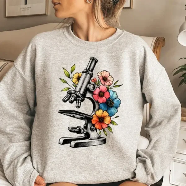 Microscopio illustrato con fiori colorati su una felpa grigia, combinando scienza e natura in uno stile moderno e alla moda.