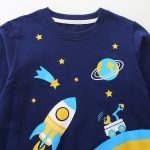 Abbigliamento per bambini con motivo spaziale, comprendente un razzo, stelle, un pianeta e un telescopio, perfetto per gli amanti dell'astronomia e dell'esplorazione spaziale.