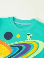 Maglietta color turchese con stampa di un astronauta e pianeti colorati, perfetta per appassionati di scienza e spazio, ideale come decorazione scientifica originale e divertente.