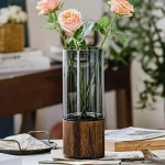 Fioriera decorativa con rose in vaso di vetro e base in legno, perfetta come oggetto scientifico decorativo.