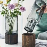 Vaso di vetro con fiori di rosa e foglie verdi, supportato da base in legno naturale, decorazione elegante e moderna per la casa o l'ufficio.